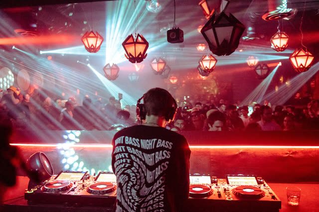 Night Bass set shot from behind the booth, lasers over a packed room